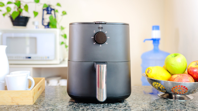 Black air fryer sitting on kitchen countertop next to bowl of fruit
