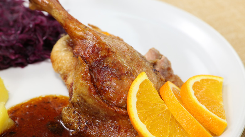 A plate of roasted duck leg with orange sauce