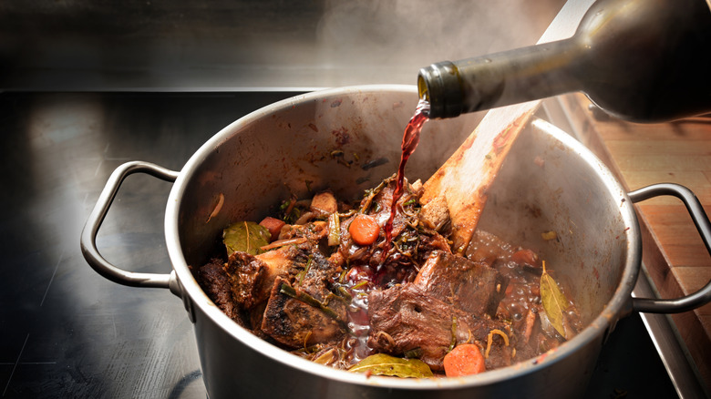 Wine being poured into a pot of stew to deglaze it