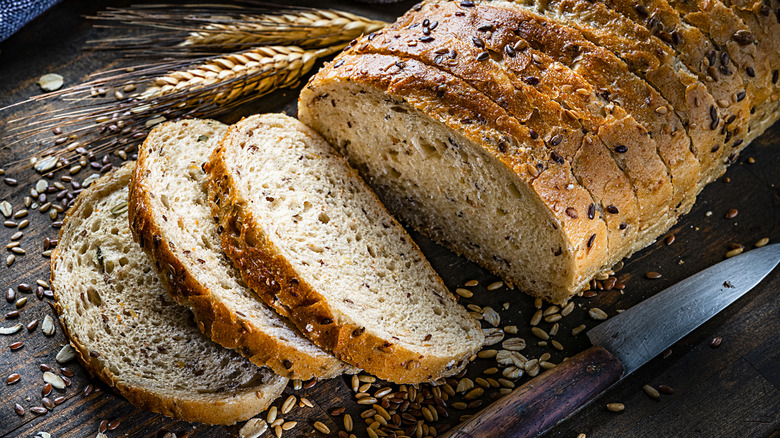 sliced whole grain bread on board with wheat and knife on the side