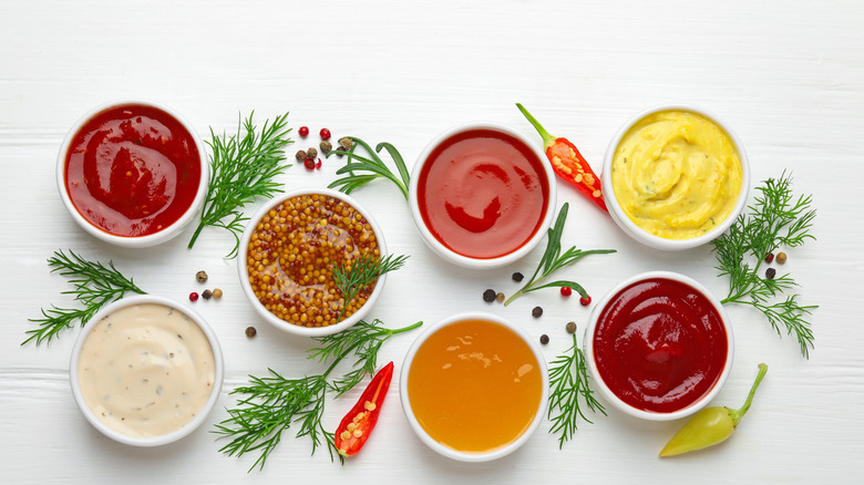 top view of various condiments in bowls on table with green herbs and spices in between