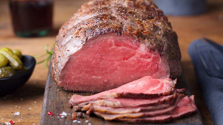 close up of whole roast beef with slices on a wooden cutting board