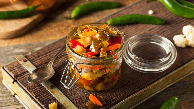 Giardiniera in jar on cutting board with some fresh veggies placed around it