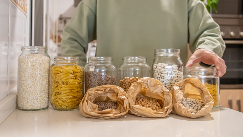 Person holding glass jar with non-perishable food items on counter