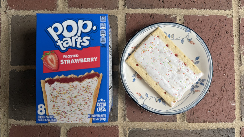 Box of frosted strawberry Pop-Tarts next to unwrapped pastry with a few sprinkles on plate