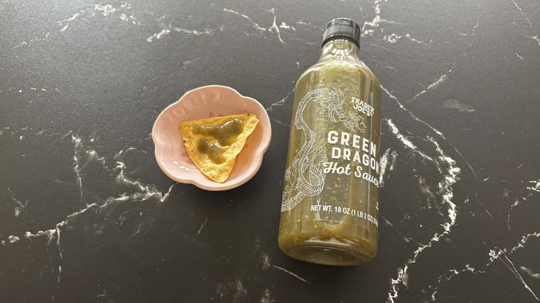 Trader Joe's green dragon hot sauce bottle next to tortilla chip with sauce on it