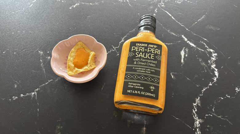 Trader Joe's peri-peri sauce bottle next to tortilla chip on small plate with drizzle of sauce