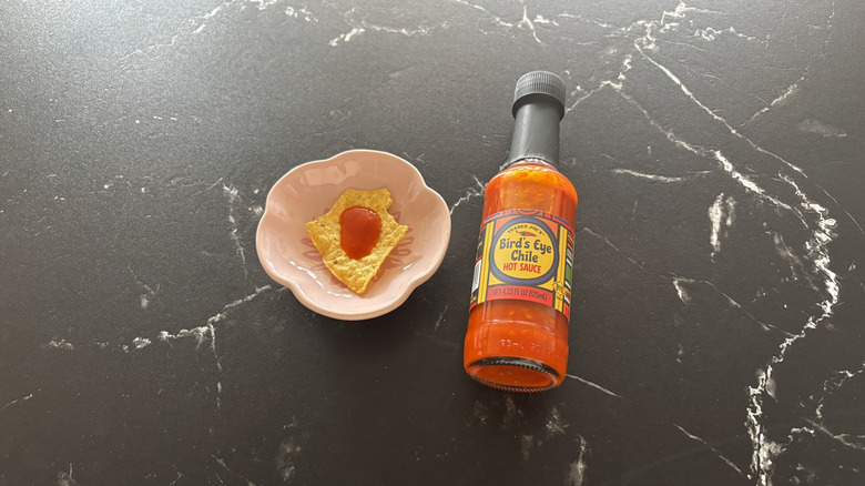Trader Joe's bird's eye chile hot sauce bottle next to tortilla chip on small plate with drizzle of hot sauce