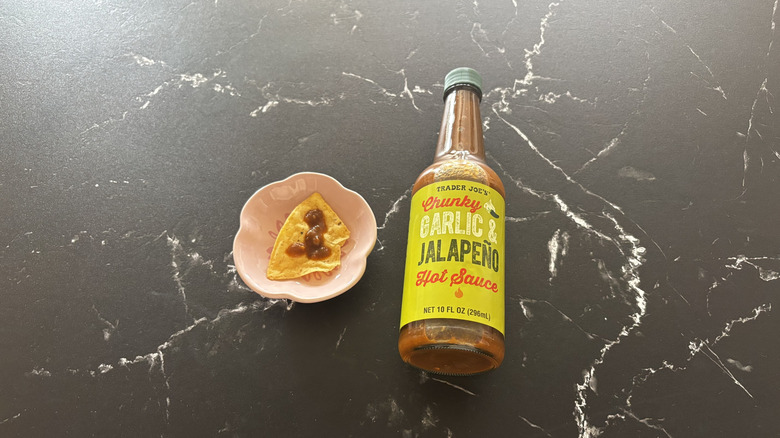 Trader Joe's chunky garlic jalapeño hot sauce bottle next to tortilla chip on plate with hot sauce drizzle