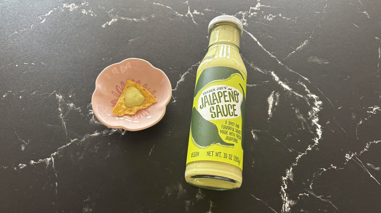 Trader Joe's jalapeño sauce bottle next to tortilla chip on plate with drizzle of sauce