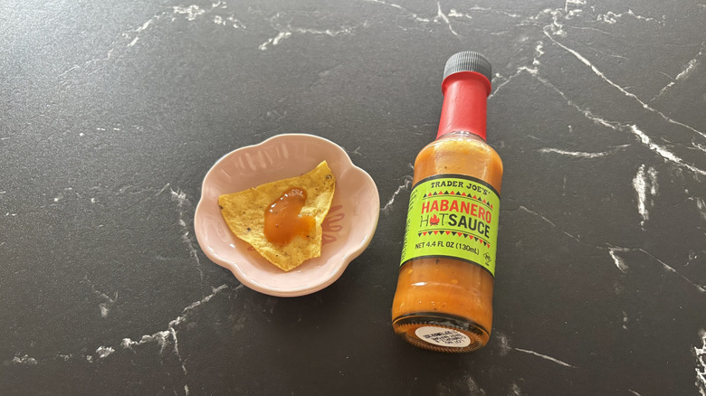Trader Joe's habanero hot sauce bottle next to tortilla chip on plate