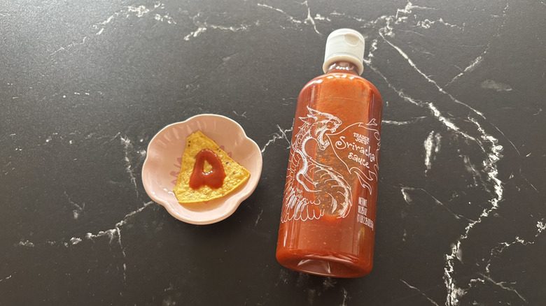 Trader Joe's sriracha hot sauce bottle next to tortilla chip on plate with drizzle of sauce