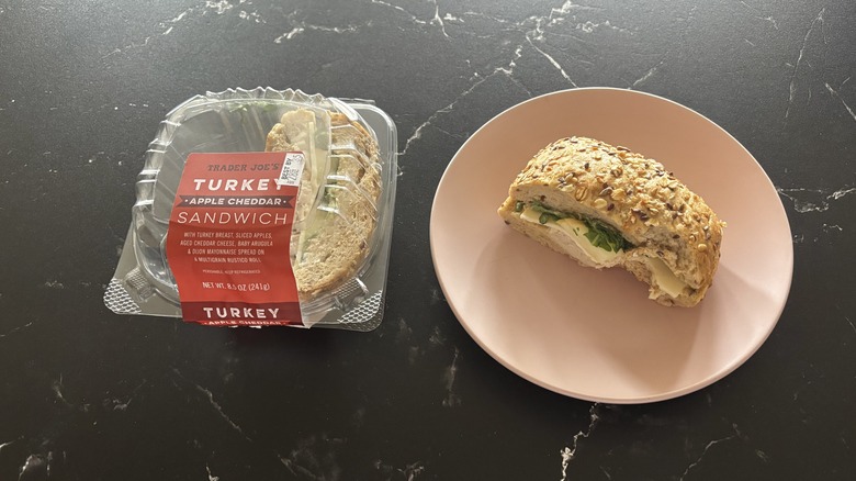 Trader Joe's turkey apple cheddar sandwich container next to half sandwich on plate