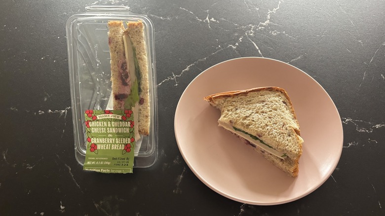 Trader Joe's chicken cheddar sandwich on cranberry bread container next to half sandwich on plate