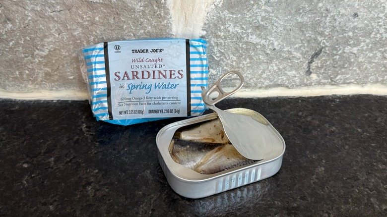 Half opened tin of sardines in spring water from Trader Joe's sitting on a black counter next to the package