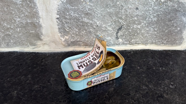 Tin of lightly smoked mussels from Trader Joe's on a dark counter in front of a gray wall