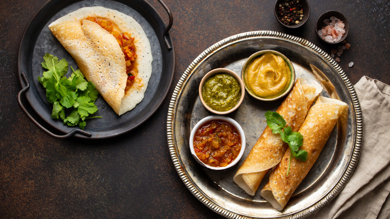Overhead view of different types of dosa with chutneys and cilantro