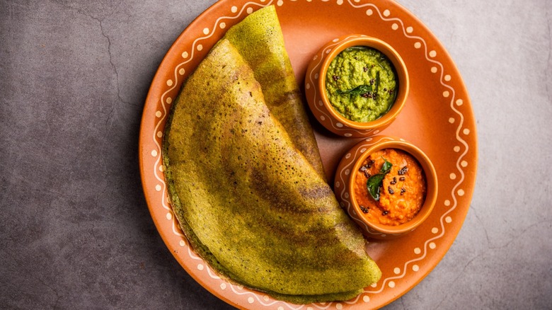 Two pesaratlu served with two chutneys on clay plate