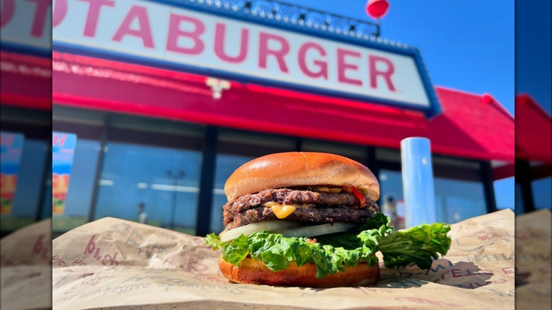A double cheeseburger on paper outside in front of a Blake's Lotaburger