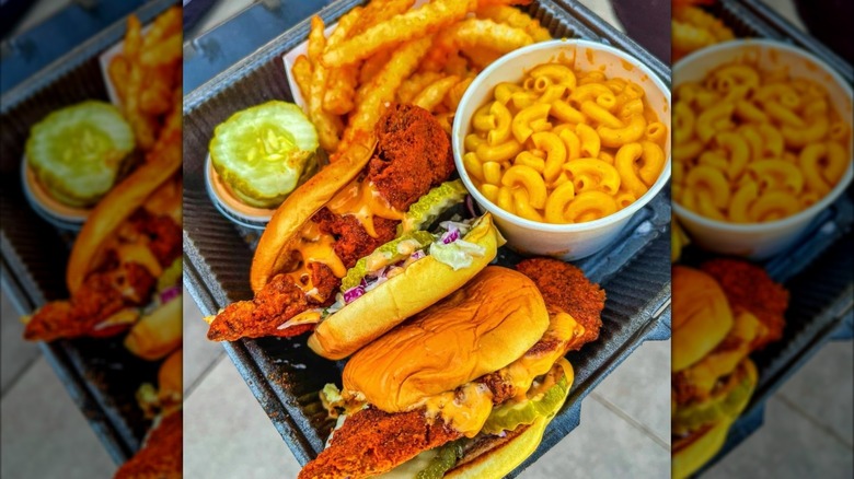 Two hot chicken sandwiches, a cup of mac and cheese, and fries in a black take out container