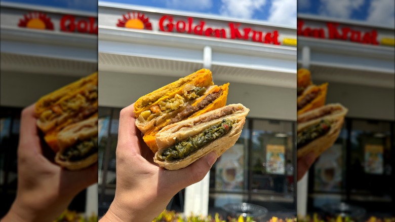 A hand holding a variety of Jamaican patties in front of a Golden Krust