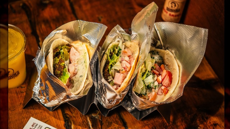 Three different pita sandwiches on a wood table at Mamoun's Falafel