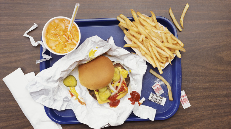 A sloppy burger on paper, fries, and a drink on a blue fast food tray