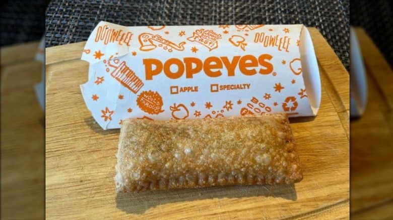 Popeye's cinnamon apple pie with wrapper on wooden cutting board