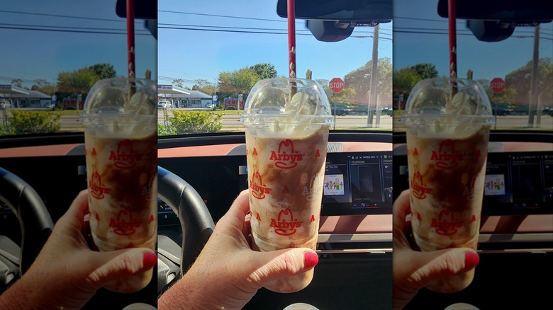 Hand holding Arby's Jamocha shake in car