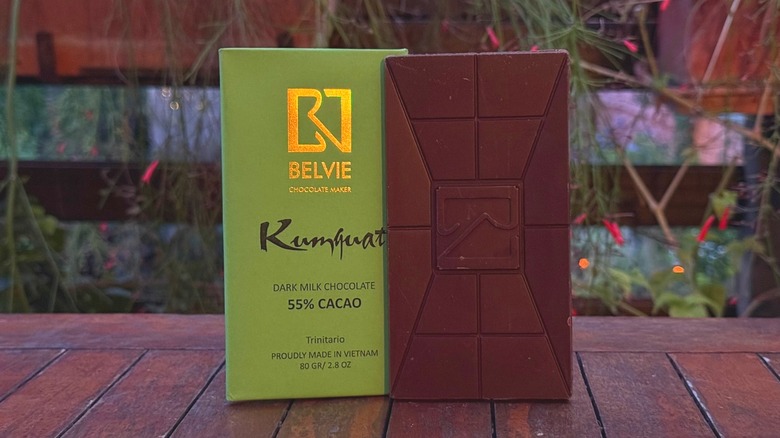 Bar of kumquat dark chocolate standing vertically next to package on wooden table