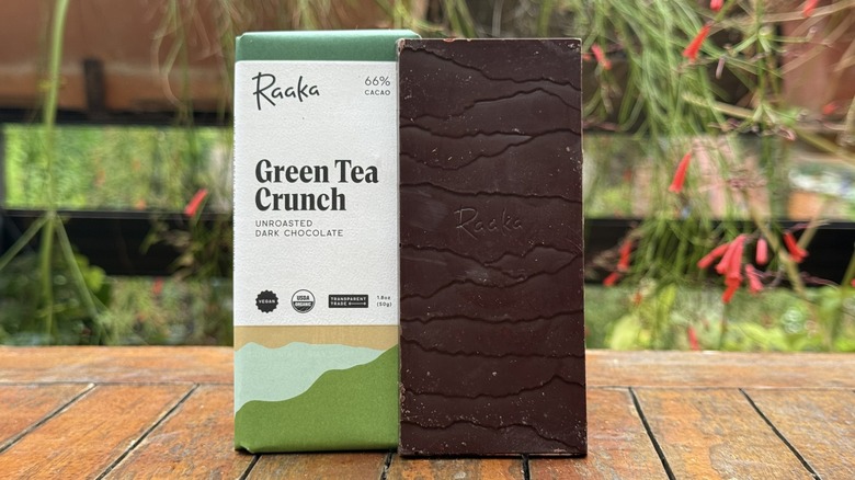 Bar of green tea crunch chocolate standing vertically next to packaging on wooden table