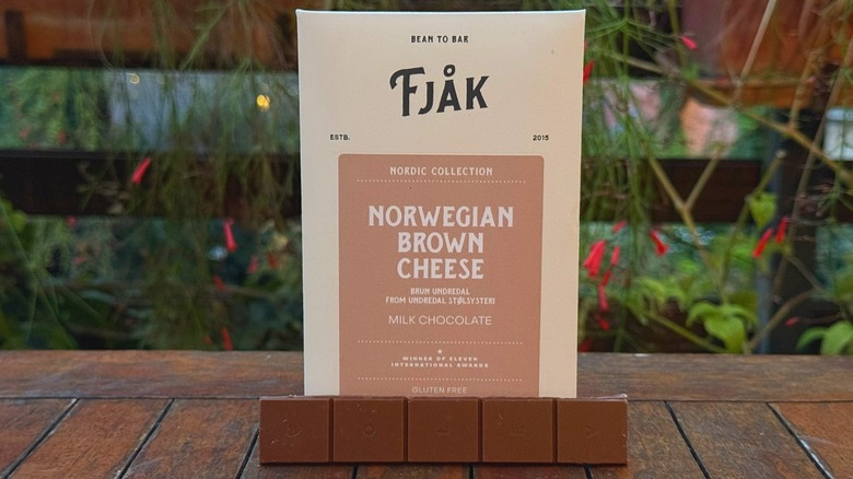 Rectangle of brown cheese chocolate resting at bottom of packaging on wooden table