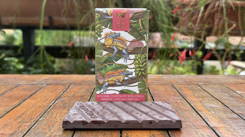 Bar of green banana chips and pink salt chocolate beneath packaging on wooden table