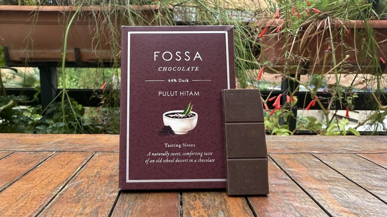 Rectangle of pulut hitam chocolate standing vertically beside packaging on wooden table