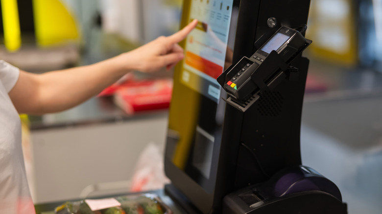 Hand pressing self-checkout screen at grocery store