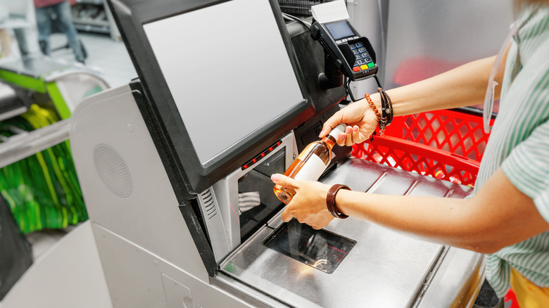 Person scanning a bottle of wine at a self-checkout station