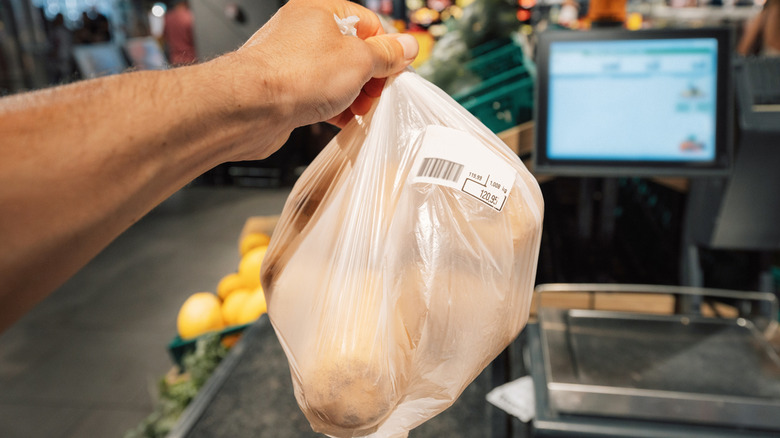 Hand holding plastic bag of produce in front of self-checkout machine