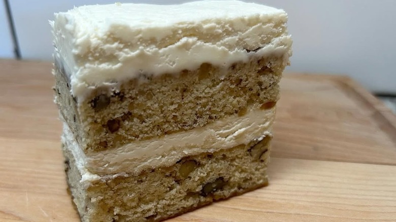 Slice of frosted black walnut cake on wooden platter