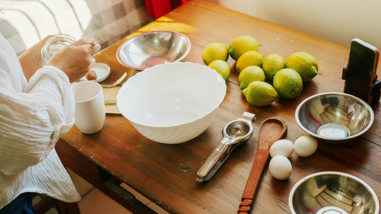 Woman preparing cake at a table laden with lemons, eggs, and bowls