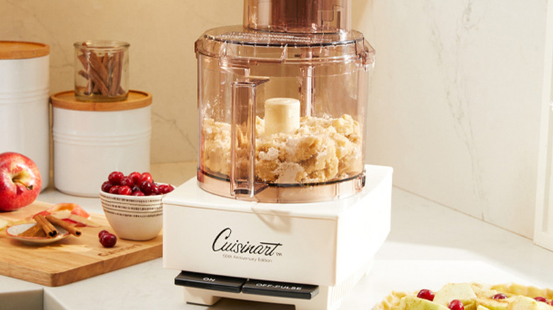 vintage marketing image of an early 1970s Cuisinart food processor, turning stale bread into crumbs, on a kitchen countertop with fruit, spices, and ingredients canisters