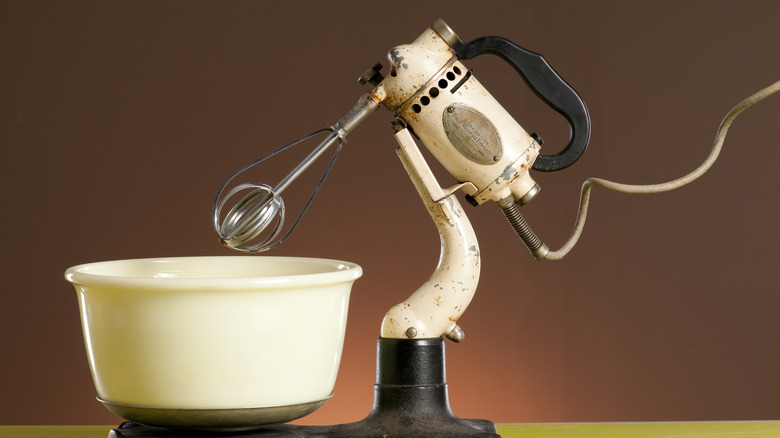 A very early stand mixer, shown against a brown background