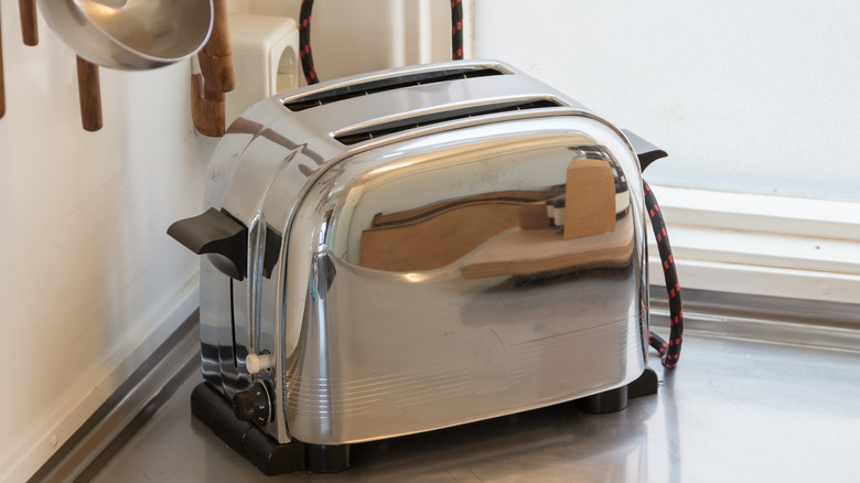 beautiful chromed-steel vintage toaster, shown in the corner of a kitchen counter near a window, with hanging utensils just visible at the top left