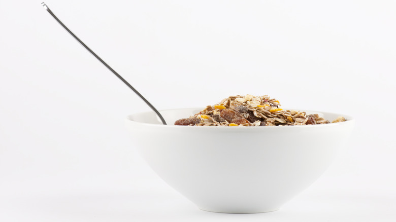 Brown flakey cereal in a white bowl with a spoon in it isolated on a white background