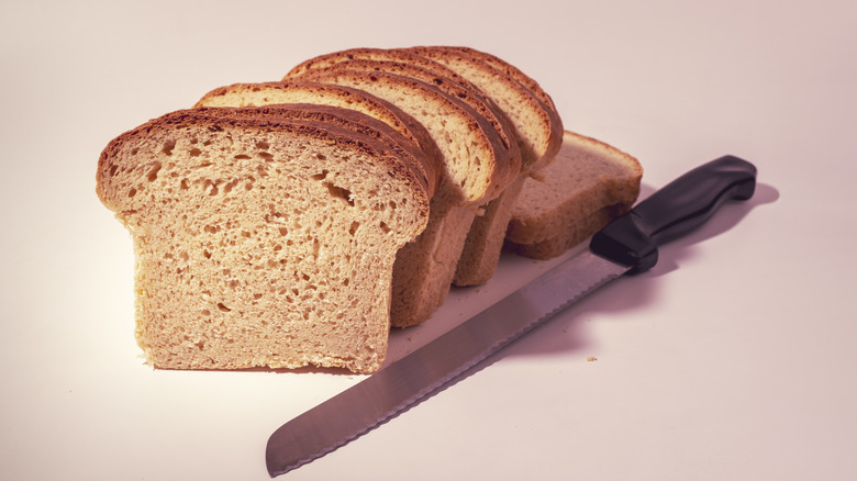 Sliced bread next to a bread knife on a vintage-looking white background