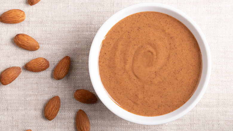 Brown almond butter in a white bowl on linen fabric
