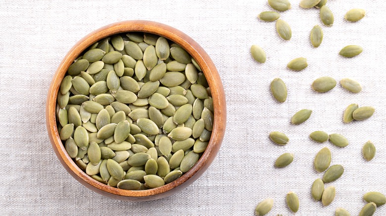 Hulled pumpkin seeds in a wooden bowl on linen