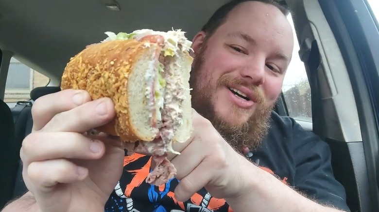 Person holding halved Jersey Mike's tuna and beef sub in a car