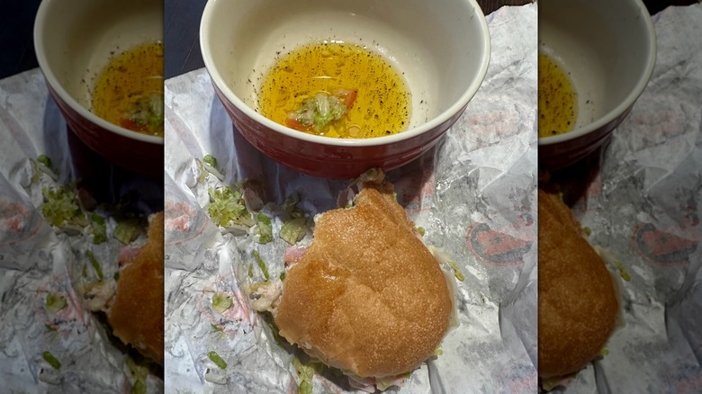 Bitten piece of Jersey Mike's sub next to bowl of oil and vinegar mixture
