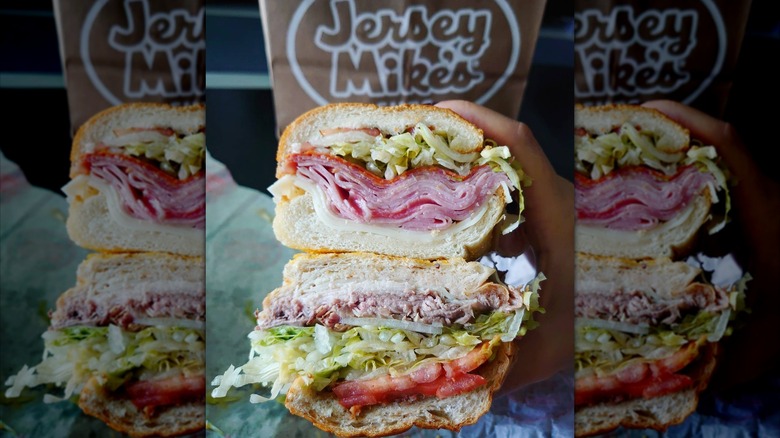Stacked halves of a Jersey Mike's sub, showing cross section of cured meat, cheese, lettuce, and tomato fillings