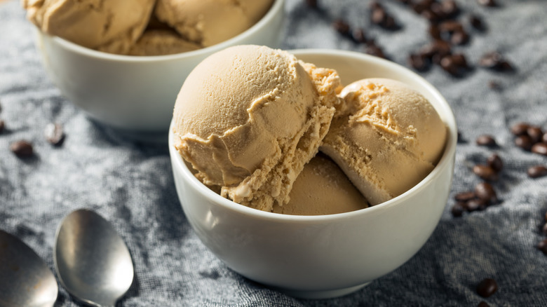 Two bowls filled with coffee ice cream, surrounded by coffee beans and spoons